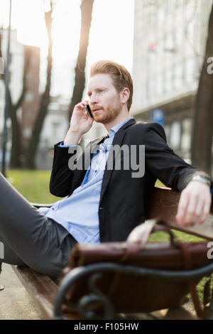 Geschäftsmann, sitzen auf einer Bank und in schöner Sonnenschein am Telefon sprechen Stockfoto