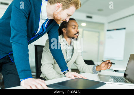 Ein schwarzer junge Mann mit Dreadlocks und ein junger hübscher roten Haaren Geschäftsmann diskutieren Grafiken Designfehler in ein schönes weißes o Stockfoto