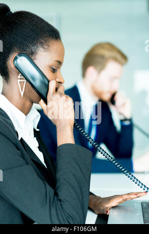 Eine schöne, schwarze, junge Frau arbeitet in einem Callcenter in einem Büro mit ihrem roten Haird Partner am anderen Ende des Schreibtisches ta Stockfoto