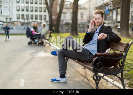 Überprüfen der Zeit Blick auf seine Uhr an einem sonnigen Tag in einem Stadtpark Geschäftsmann Stockfoto