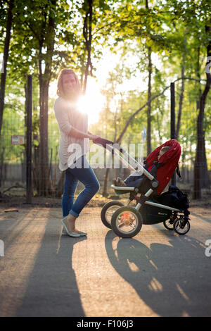 Mutter zu Fuß Kind in einem Kinderwagen im park Stockfoto