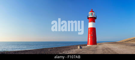Ein rot-weißen Leuchtturm auf dem Meer unter strahlend blauem Himmel. Fotografiert in der Nähe von Westkapelle in Zeeland, Niederlande. Stockfoto