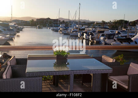 Bild ein eleganter Tisch und Stühle vor einer Marina voll von luxuriösen Yachten, am Abend Stockfoto