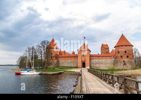 Vorderansicht der Burg Trakai mit Holzbrücke auf verschlossen und kleine Boote in See, am bewölkten Himmelshintergrund. Stockfoto