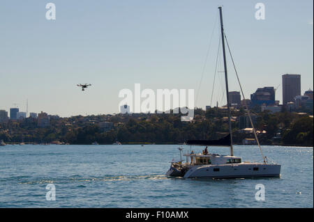 Eine Drohne mit Kamera schwebt über einer Yacht, wie es durch Sydney Harbour in Australien Motoren Stockfoto