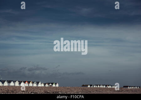 Reihe von Strandhütten auf einem Kiesstrand sind beleuchtet, von der Frühlingssonne in Ferring, West Sussex. Stockfoto