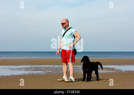 Mann und sein Labradoodle Hund spielen am Strand in Blackpool, Lancashire Stockfoto