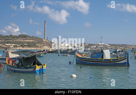 Bunte farbenfrohe traditionelle Fischerboote mit Power Station jenseits, Fischerdorf Marsaxlokk, Malta. Stockfoto