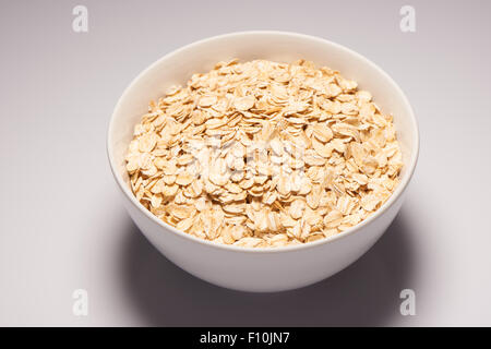 Rohe Bio Haferflocken Flakes in weißer Keramik Schüssel auf weißem Hintergrund Stockfoto