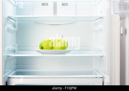 Zwei grüne Äpfel auf weißen Teller in offenen leeren Kühlschrank. Gewicht-Verlust-Diät-Konzept. Stockfoto