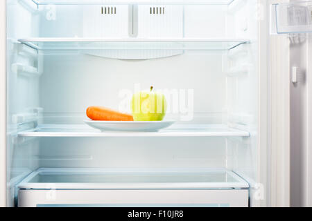 Grüner Apfel und orange Karotten auf weißen Teller in offenen leeren Kühlschrank. Gewicht-Verlust-Diät-Konzept. Stockfoto