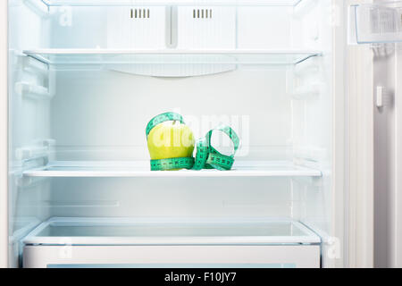 Grüner Apfel mit Maßband auf Regal öffnen leeren Kühlschrank. Gewicht-Verlust-Diät-Konzept. Stockfoto