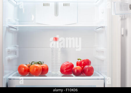 Zweig der rote Tomaten, 2 rote Paprika, zwei zweifarbig orange und rote Pfirsiche und eine Flasche Wasser auf Regal offen leer ref Stockfoto