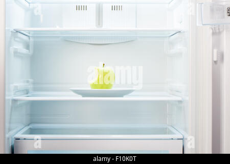 Grüne angebissene Apfel auf weißen Teller in offenen leeren Kühlschrank. Gewicht-Verlust-Diät-Konzept. Stockfoto