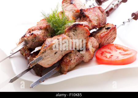 Frisch gebratene Fleischstücke am Spieß, Verlegung auf einem weißen Teller mit Tomaten und Dill auf weißem Hintergrund Stockfoto