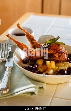 Gebratene Wachtel mit Kirsche & brandy Sauce & Fondant Kartoffelwürfel in weiße Schale mit traditionellen Silberbesteck auf Serviette serviert. Stockfoto