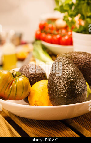 Obstschale auf Küchentisch, mit Avocados, Zitronen und Erbe Tomaten. Stockfoto