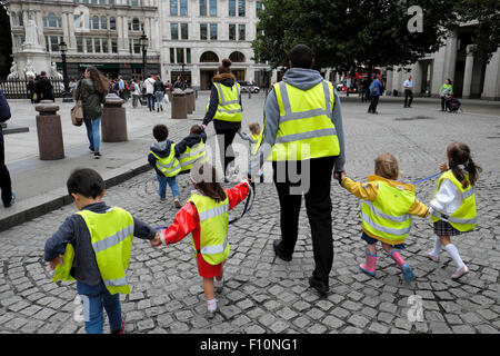 Britische Kindergärtnerinnen und -Kinder, die eine gut sichtbare fluoreszierende Sicherheitsjacke tragen, halten die Hände an der Walkman London Street UK KATHY DEWITT Stockfoto