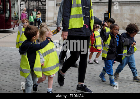 Kindergarten Kinder & Tagesmutter tragen hohe Sichtbarkeit fluoreszierende Warnwesten halten die Hände auf Spaziergang in einer Straße in London UK KATHY DEWITT Stockfoto