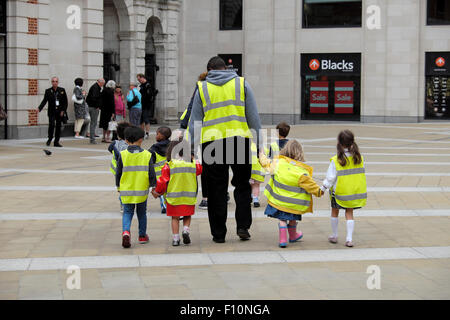 Kindergarten Kinder wandern mit tagesmütter tragen hohe Sichtbarkeit fluoreszierende Warnwesten auf einer Straße in der Londoner City UK KATHY DEWITT Stockfoto