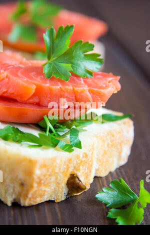 Sandwich mit Lachs (Forelle), Frischkäse, Tomaten und Petersilie auf rustikalen hölzernen Hintergrund hautnah Stockfoto