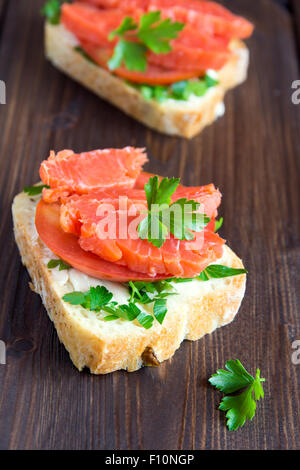 Sandwich mit Lachs (Forelle), Frischkäse, Tomaten und Petersilie auf rustikalen hölzernen Hintergrund hautnah Stockfoto