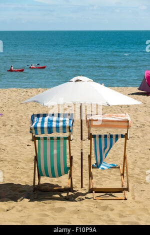 Liegestühle und ein Sonnenschirm am Strand von Sandown Isle Of Wight UK an einem sonnigen Sommertag zu schleppen Stockfoto