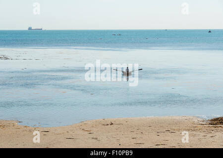 Eine Person, die ein kleines Ruderboot am Ufer Meeres bei Ebbe an Bembridge Isle Of Wight UK Stockfoto