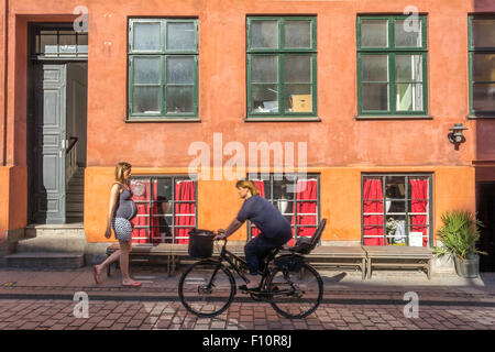 Eine schwangere Frau läuft in Kopenhagen in Dänemark auf einer farbenfrohen Kopfsteinpflasterstraße Stockfoto