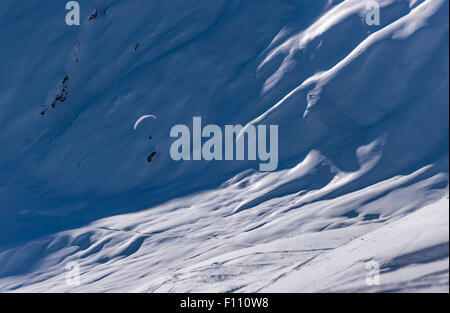 Ein Gleitschirm fliegt hoch oben in den schneebedeckten Bergen über ein Schneefeld in Belalp/Blatten, Schweiz (Kanton Wallis). Stockfoto