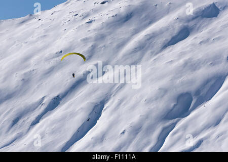 Ein Gleitschirm fliegt hoch oben in den schneebedeckten Bergen über ein Schneefeld in Belalp/Blatten, Schweiz (Kanton Wallis). Stockfoto