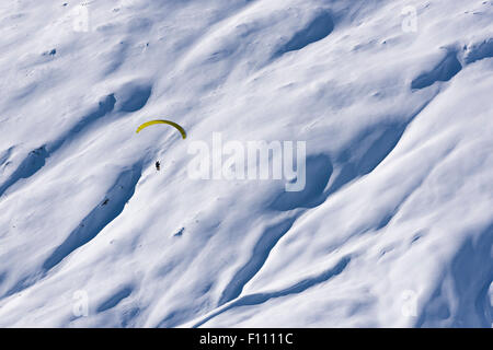 Ein Gleitschirm fliegt hoch oben in den schneebedeckten Bergen über ein Schneefeld in Belalp/Blatten, Schweiz (Kanton Wallis). Stockfoto