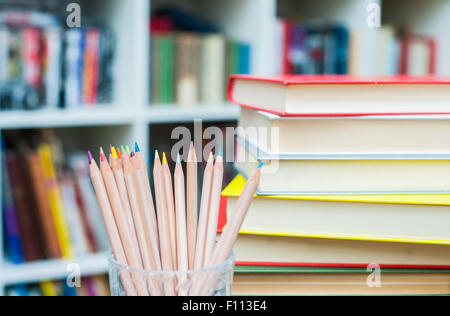 Buntstifte in Glas Stifthalter mit Stapel Bücher im Hintergrund unscharf Stockfoto