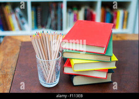 Buntstifte in Glas Stifthalter mit Stapel Bücher mit verschiedenen Farben deckt Stockfoto