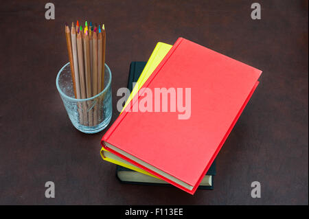 Buntstifte und Stapel Bücher mit rotem Einband auf hölzernen desktop Stockfoto