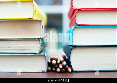 Reihe von Buntstiften auf hölzernen Schreibtisch zwischen zwei Stapel von Büchern selektiven Fokus Stockfoto