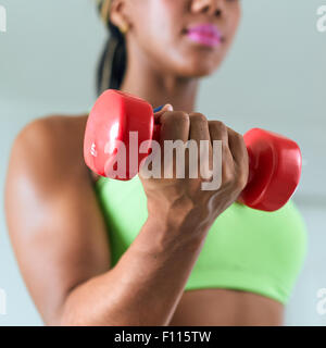 Junge afrikanische amerikanische Frau im Sport Kleidung zu Hause, häusliche Fitness zu tun und training Bizeps mit Gewicht. Im Fokus Stockfoto