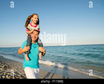 Hispanische Vater Tochter auf den Schultern am Strand tragen