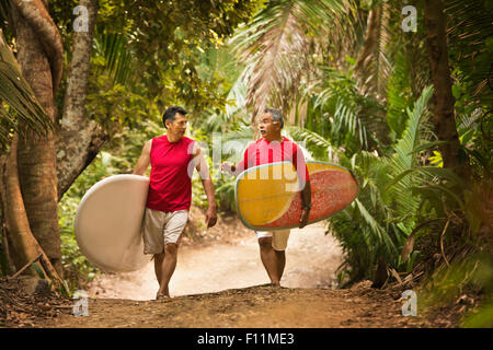 Hispanische Männer tragen Surfbretter auf Dschungelpfad Stockfoto