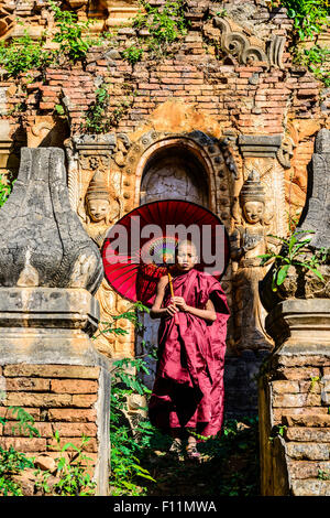 Asiatischer Mönch in der Ausbildung mit Sonnenschirm zu Fuß auf buddhistischen Schrein Stockfoto