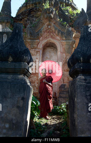 Asiatischer Mönch in der Ausbildung mit Sonnenschirm zu Fuß auf buddhistischen Schrein Stockfoto