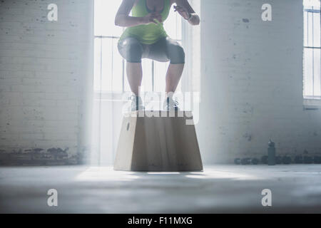 Athlet kauert auf Plattform im Fitness-Studio Stockfoto