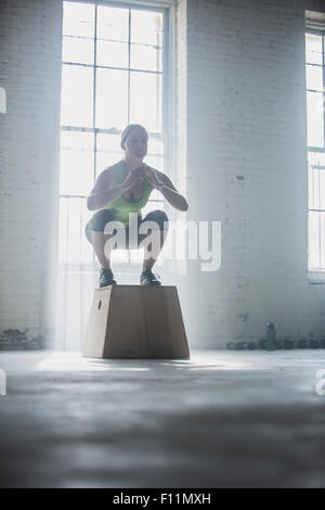 Athlet kauert auf Plattform im Fitness-Studio Stockfoto