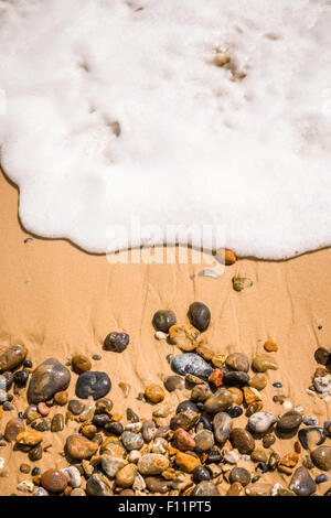 Eine Welle wäscht über Kieselsteine am Strand Suffolk. Stockfoto