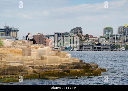 Menschen sitzen auf und genießen einige der 10.000 Sandsteinblöcke, die vor Ort geschnitten und entlang des Wasserrands des Barangaroo Headland Reserve, Sydney, verwendet wurden Stockfoto