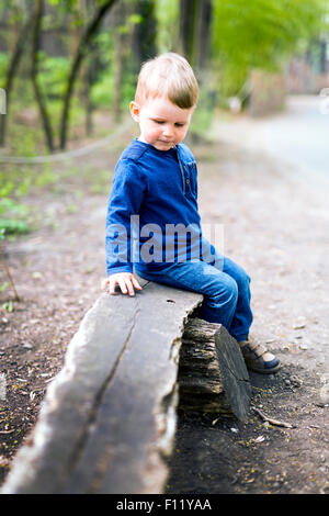 Niedliche kleine Junge sitzt auf einer Holzbank Stockfoto