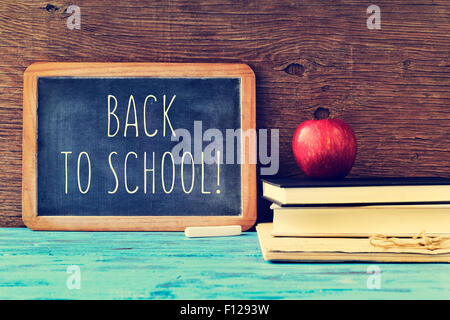 eine Tafel mit dem Text zurück zur Schule, ein Stück Kreide und ein roter Apfel auf einen Stapel Bücher auf einem blauen rustikalen geschrieben Stockfoto