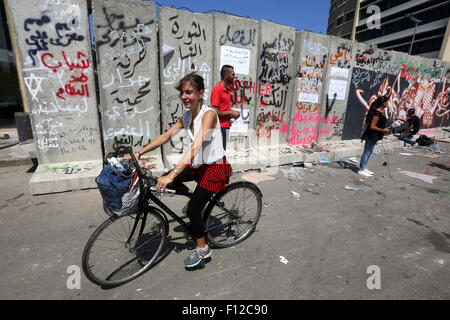 Beirut, Libanon. 25. August 2015. Eine libanesische Frau fährt Fahrrad vor einer konkreten Explosion-Wand mit Graffiti Darstellung der verschiedenen politische Gruppen und Lager Botschaften gegen Polizeibrutalität, vor der Demontage, vor dem Sitz der Regierung in zentrale Beirut am 25. August 2015 zu verbreiten. Die Mauer wurde nach heftigen Protesten errichtet, über eine Müll-Krise, die in eine Steckdose für tief sitzende Frustration über Regierung Impotenz entwickelt © Marwan Tahah/APA Bilder/ZUMA Draht/Alamy Live News Stockfoto