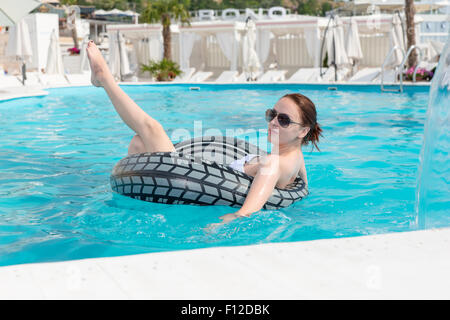 Hübsche junge Frau verwenden aufblasbare Rettungsring während Entspannung im Schwimmbad während ihre Sommerferien in einem Resort. Stockfoto