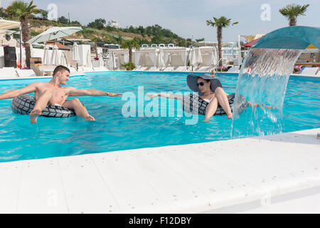 Junges Paar mit aufblasbarer Rettungsring versuchen, ihre Hände während genießen im Schwimmbad in einem Resort zu erreichen. Stockfoto